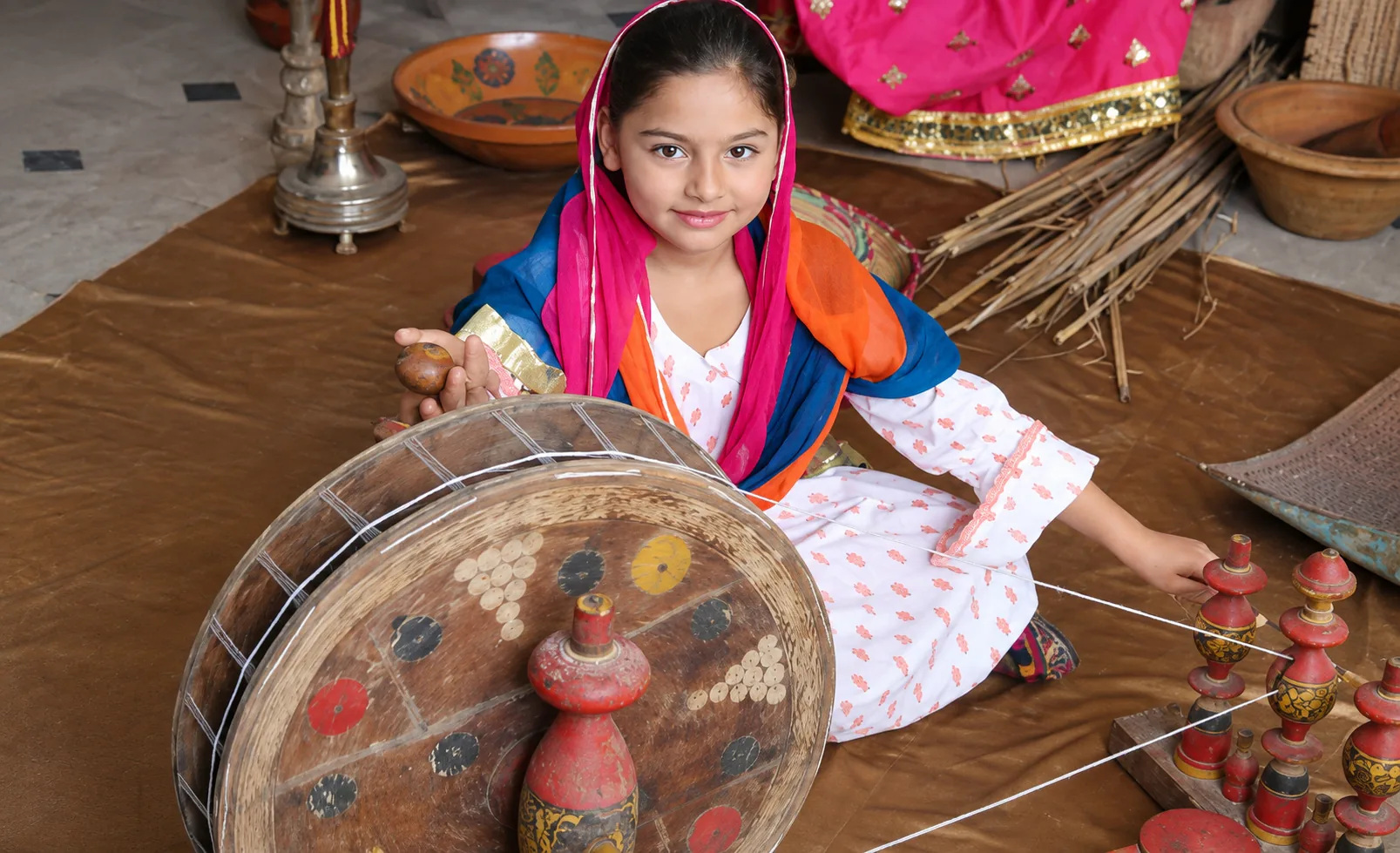 Student in traditional dress with a spinning wheel at a cultural event